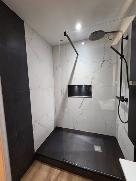 Douche moderne avec murs marbrés et éclairage intégré, sol noir.