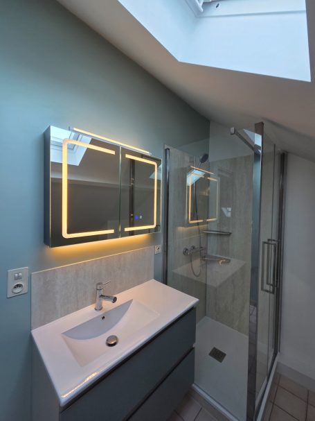 Salle de bains moderne avec lavabo, miroir lumineux et douche vitrée.
