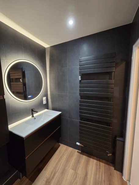 Salle de bain moderne avec un meuble noir, miroir rond et radiateur noir.