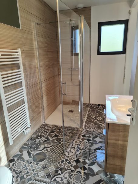 Salle de bain moderne avec douche vitrée, sol en carreaux décoratifs et meuble lavabo.