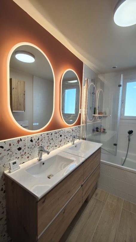 Salle de bain moderne avec un meuble en bois, deux miroirs ronds et des lumières douces.